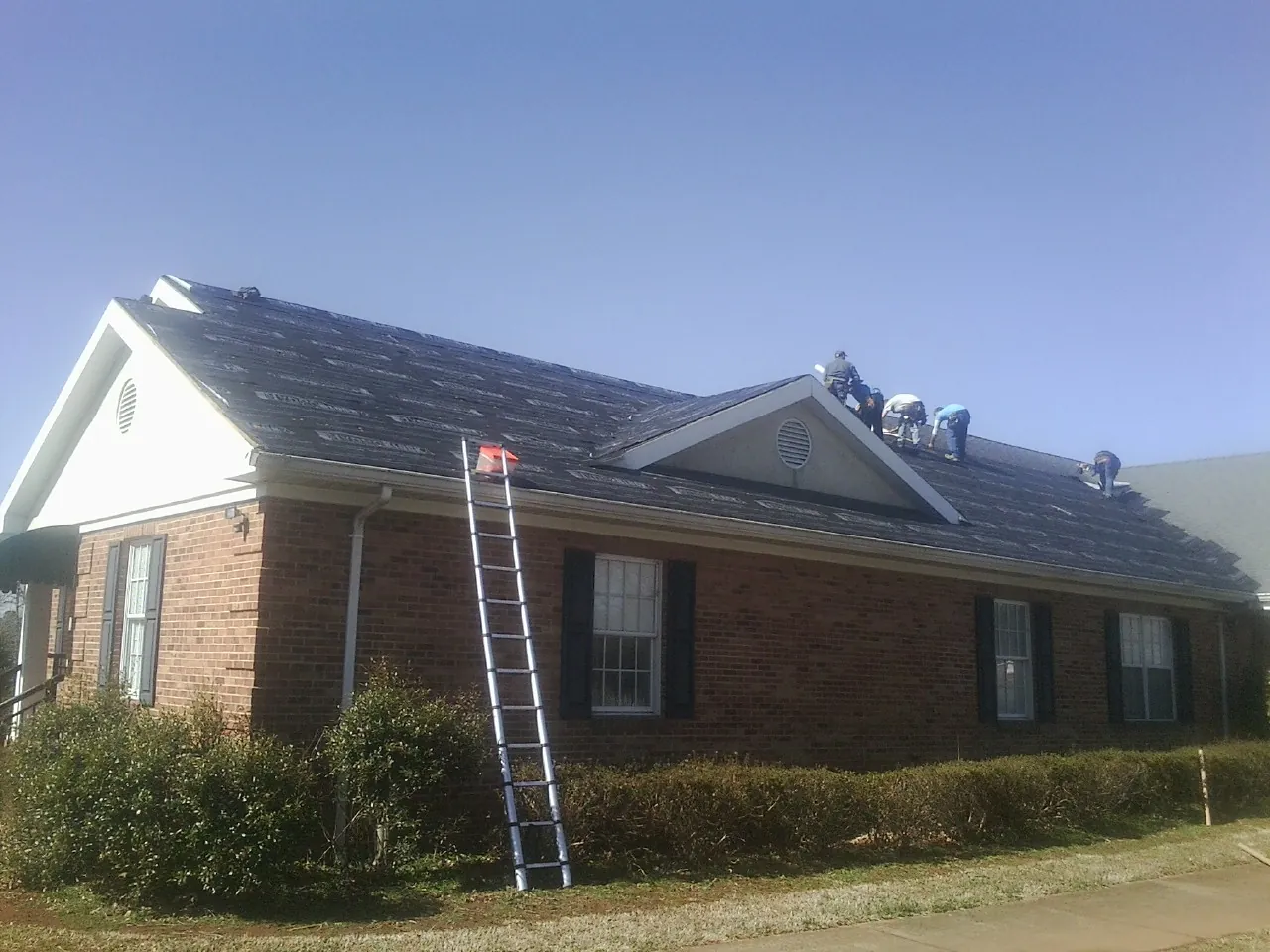 Crew tearing shingles off a brick ranch roof with a ladder set — Emergency Roof Repair work by our crew in Baltic
